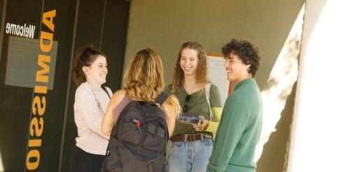 Four students chat in front of the admission office.